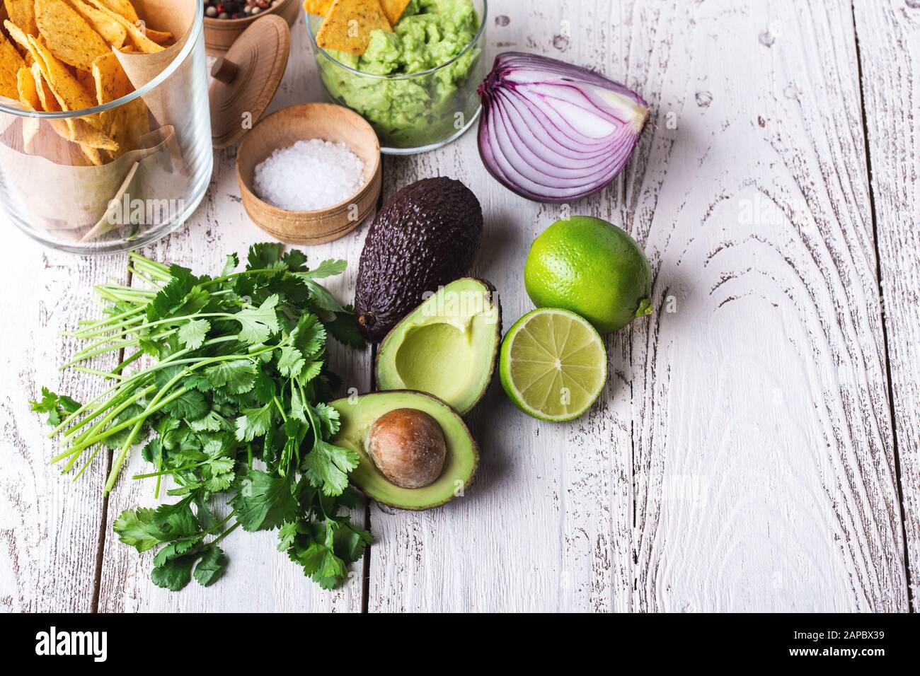 Mexican traditional food, guacamole sauce ingredients  avocado, red onion, cilantro, lime and tortilla corn chips on white rural table. Preparing loca Stock Photo
