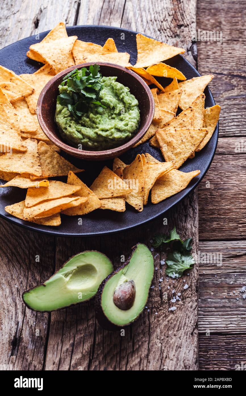 Mexican traditional food, guacamole sauce, ingredients  avocado, cilantro, lime and tortilla corn chips on wooden rural table. Preparing local plant b Stock Photo