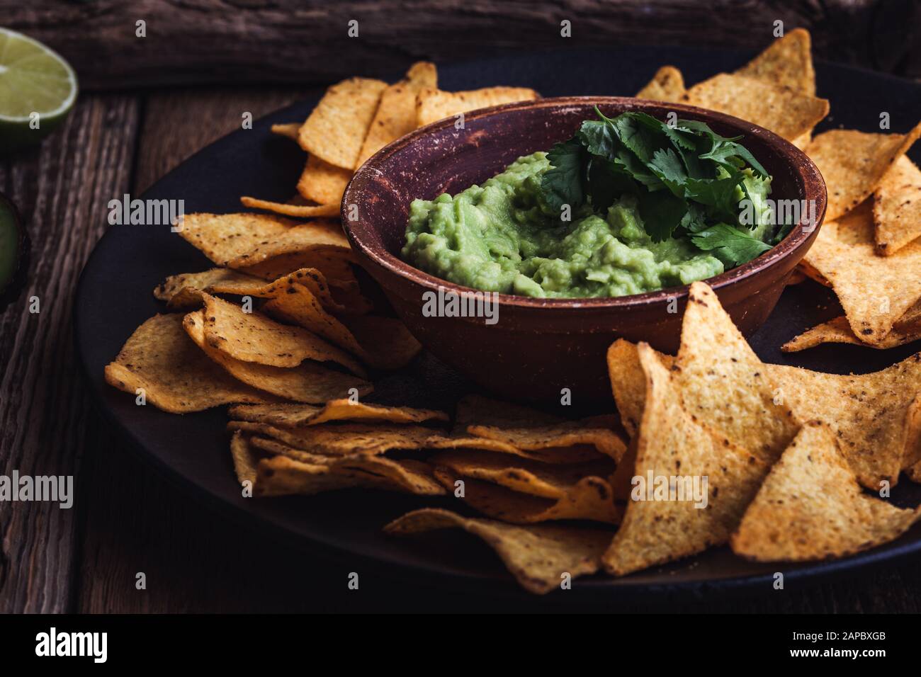 Mexican traditional food, guacamole sauce, ingredients  avocado, cilantro, lime and tortilla corn chips on wooden rural table. Preparing local food Stock Photo