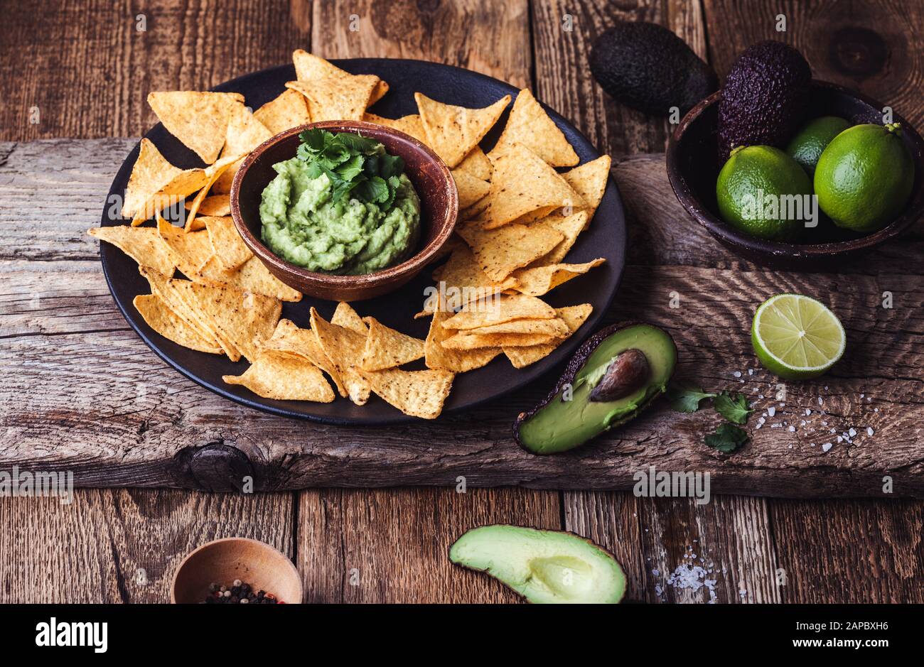 Mexican traditional food, guacamole sauce, ingredients  avocado, cilantro, lime and tortilla corn chips on wooden rural table. Preparing local food Stock Photo