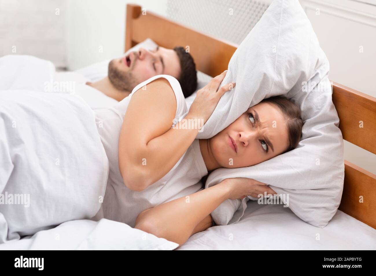 Angry Girlfriend Covering Ears Lying Near Snoring Boyfriend In Bed Stock Photo