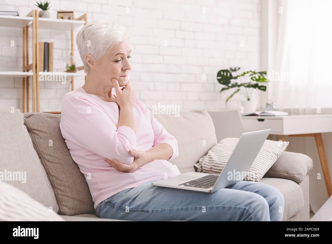 Puzzled senior lady looking at laptop with perplexity Stock Photo