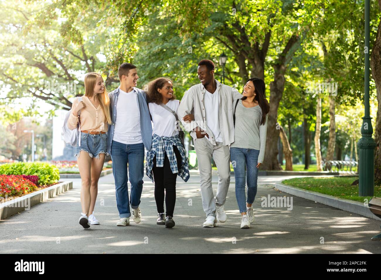 Happy students walking together in public park after studying Stock ...