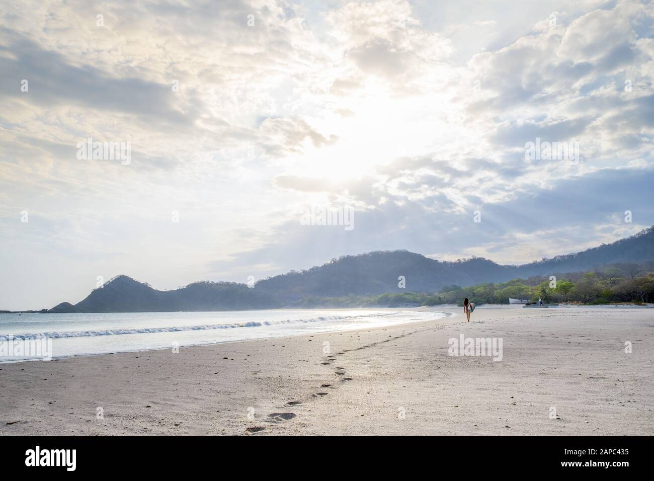 Central America, Nicaragua, San Juan del Sur. A woman surfer leaving footfalls on an empty white sand beach at sunset Stock Photo