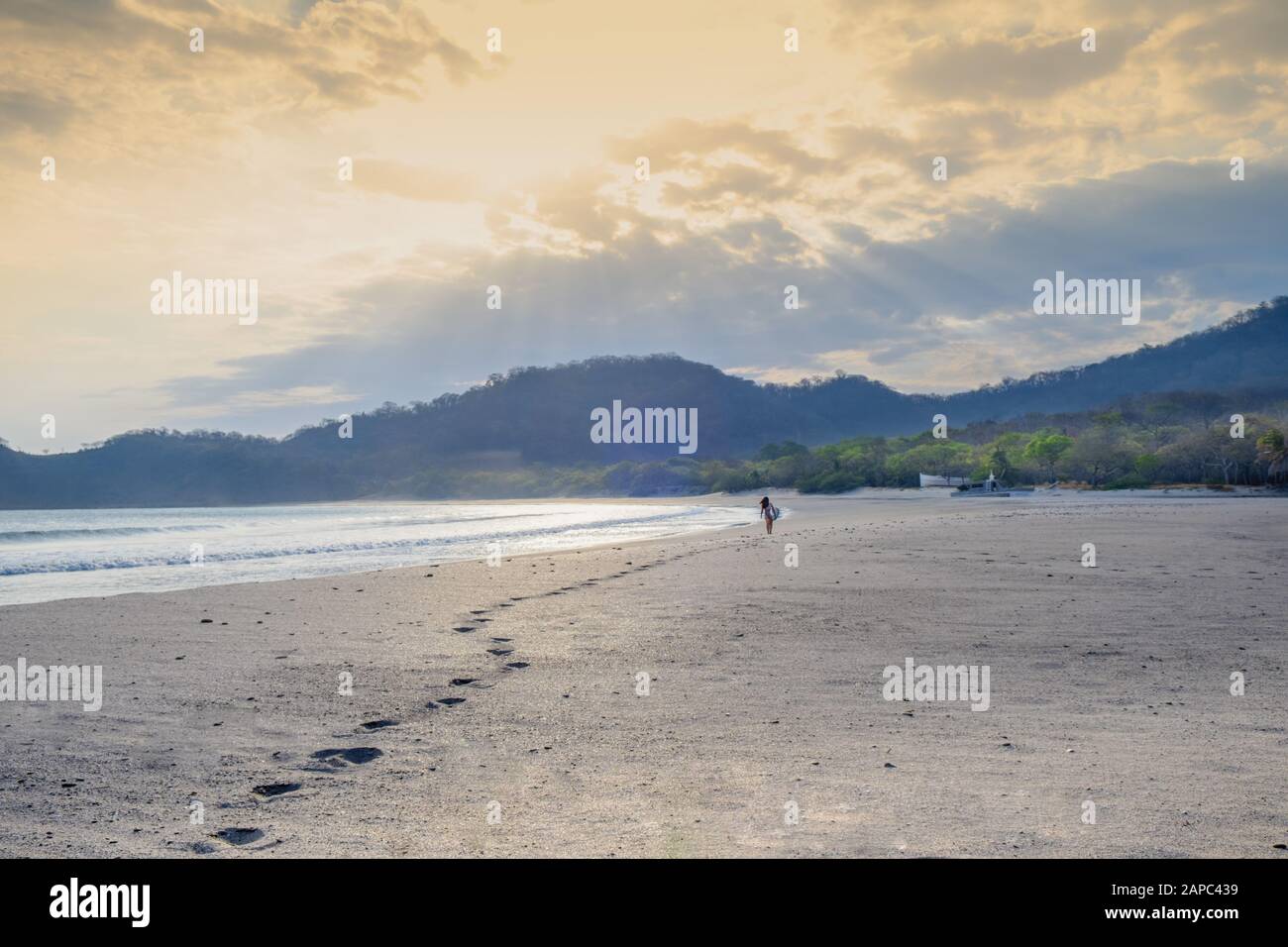 Central America, Nicaragua, San Juan del Sur. A woman surfer leaving footfalls on an empty white sand beach at sunset Stock Photo