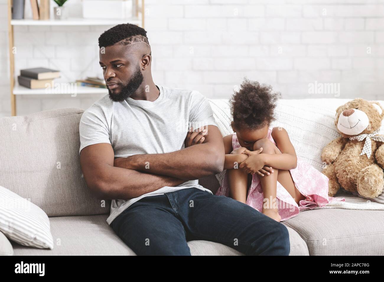 Offended black girl crying, sitting on sofa next to dad Stock Photo