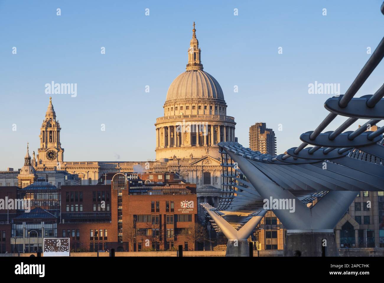 The dome of St. Paul's cathedral with the brown brick City of London private boys' school illuminated by sunlight and the Millennium pedestrian bridge Stock Photo
