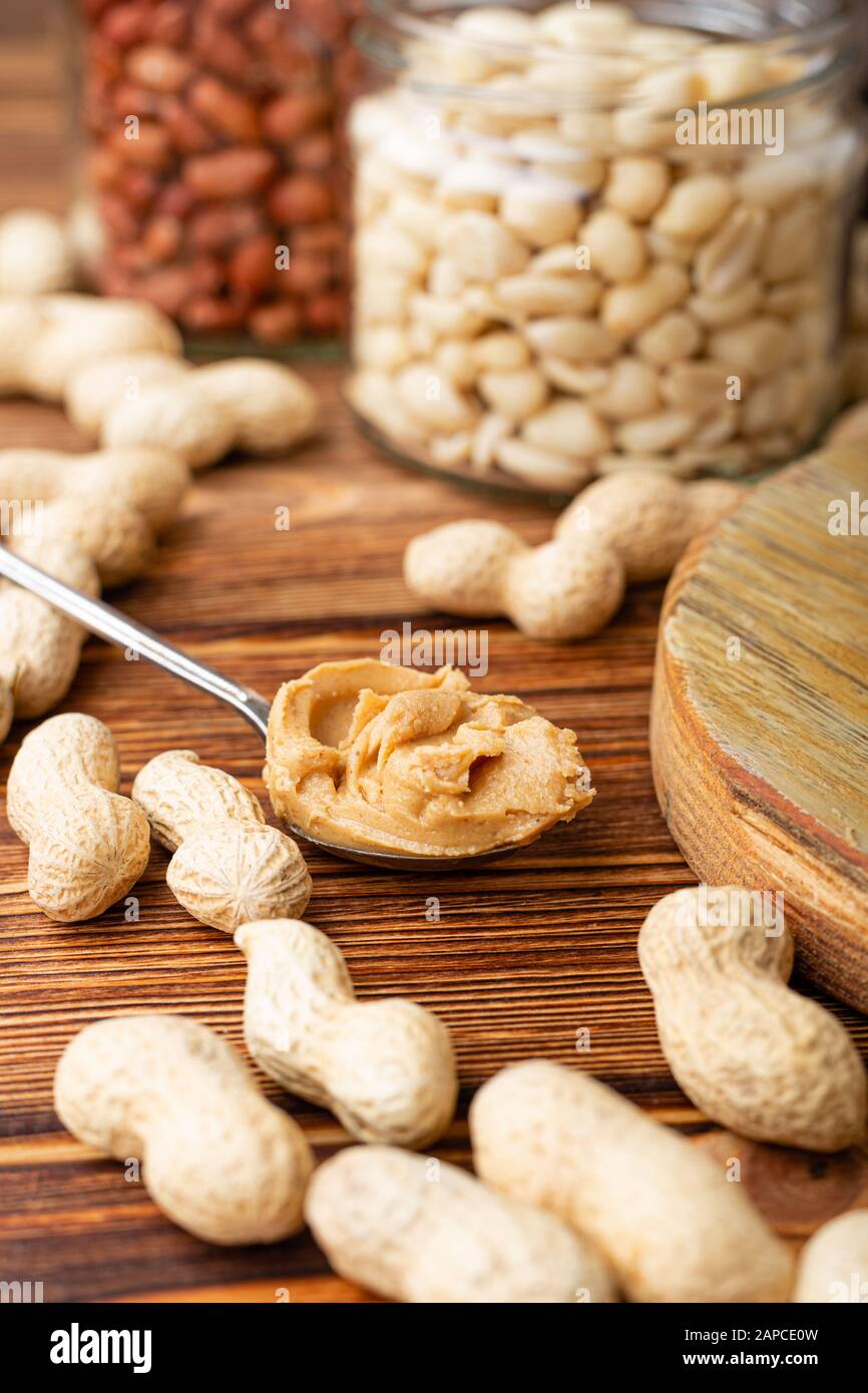 Peanut butter in spoon near peeled and inshell peanuts in jars. Peanuts