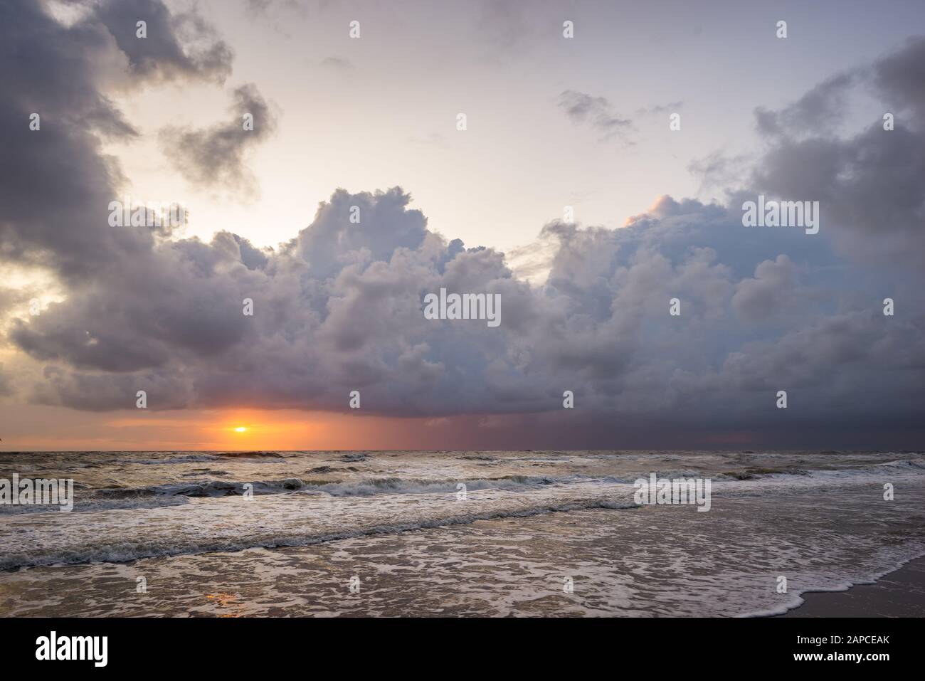 Sun sets over the sea below dramatic storm clouds Stock Photo