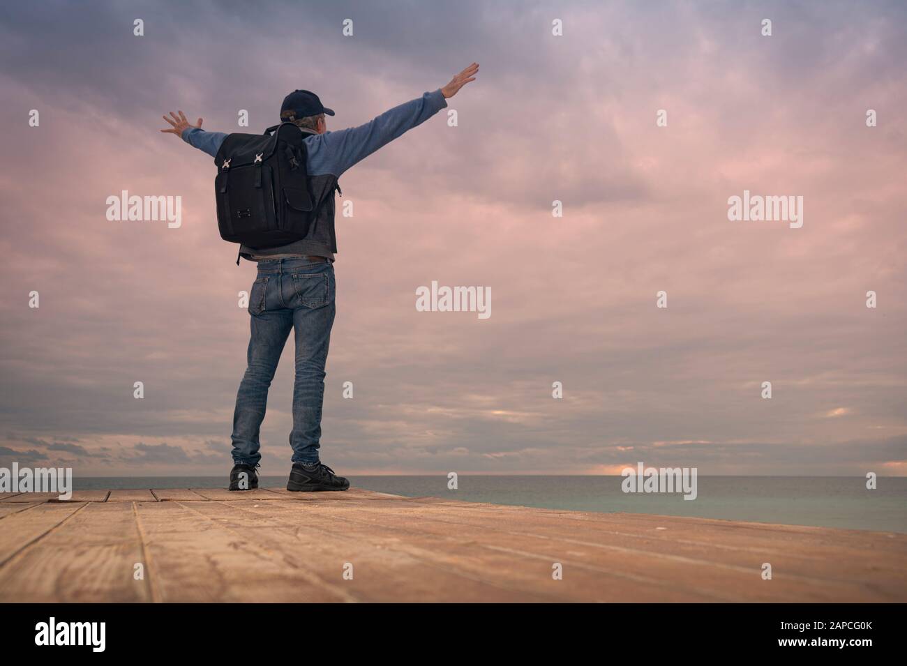 male backpacker with arms raised looking out to sea, freedom. Stock Photo