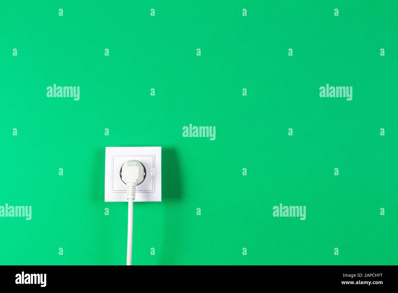 White cable plugged into electrical socket on green color background Stock Photo