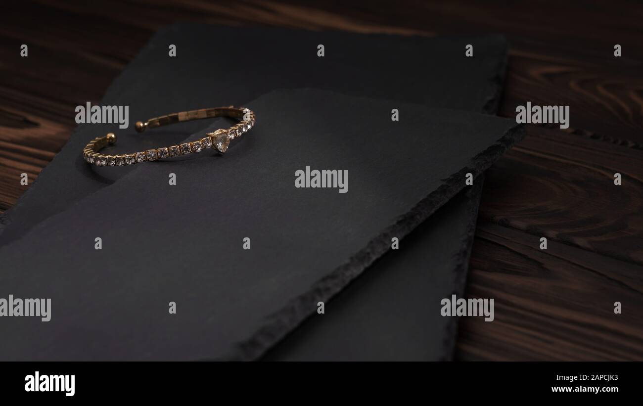 Golden with diamonds bracelet on black stone plates. Diamond golden bracelet on rough textured stone plates on wooden table. Stock Photo