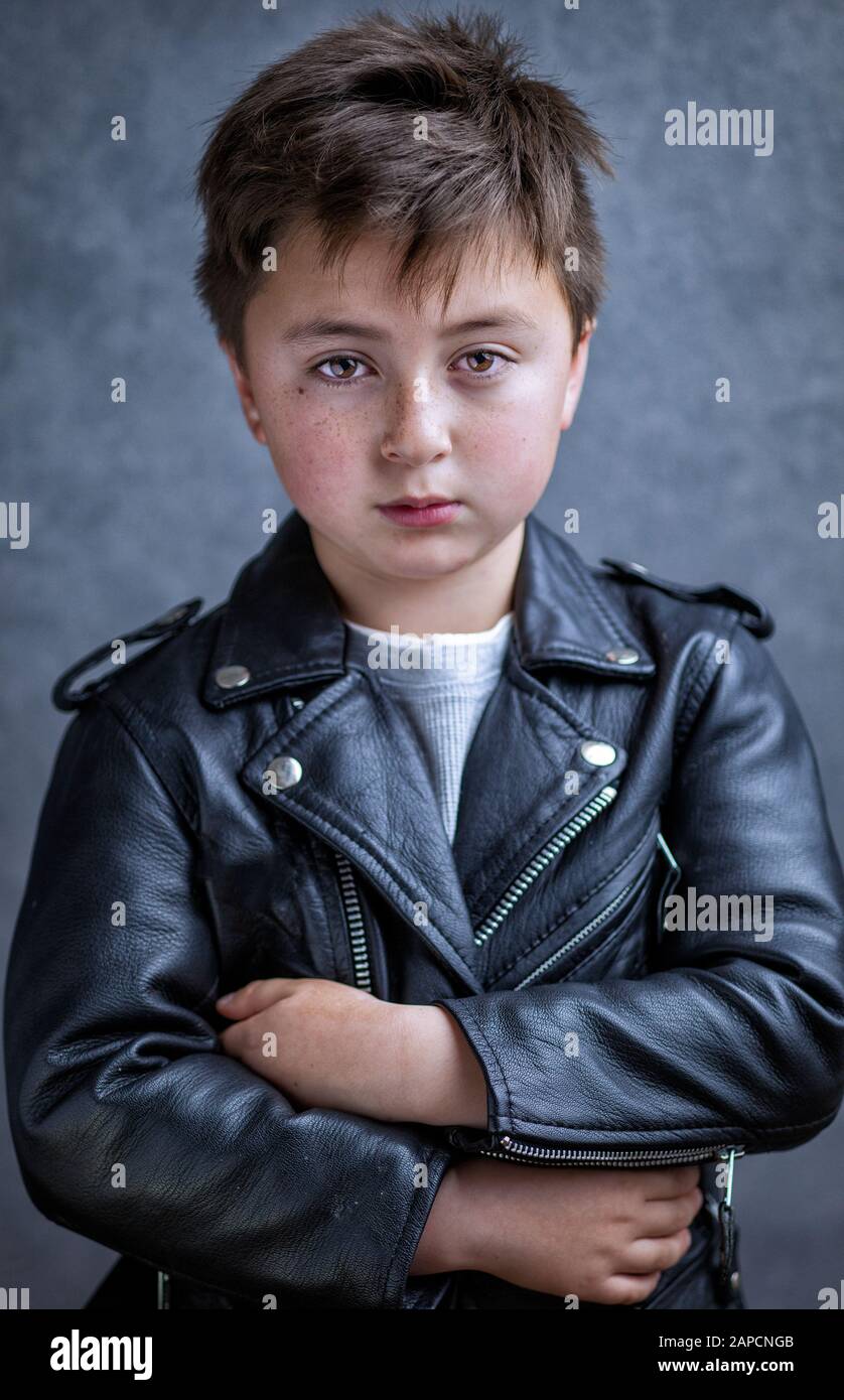 Handsome multi-racial Asian Caucasian little juvenile delinquent boy wearing a black leather motorcycle jacket with arms crossed in a defiant pose wit Stock Photo