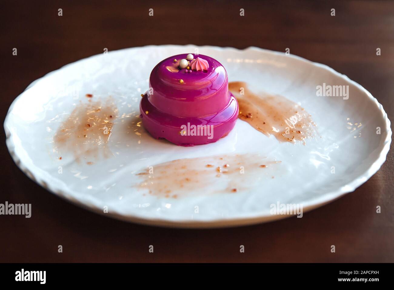 Round cake with walnut filling poured pink glaze. On a white plate, standing on the table. Stock Photo