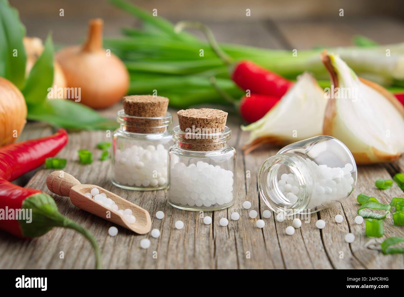 Onion bulbs, green onions, red chili peppers and bottles of homeopathic globules. Allium cepa and capsicum homeopathic remedies. Stock Photo