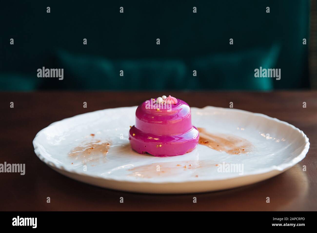 Round cake with walnut filling poured pink glaze. On a white plate, standing on the table. Stock Photo
