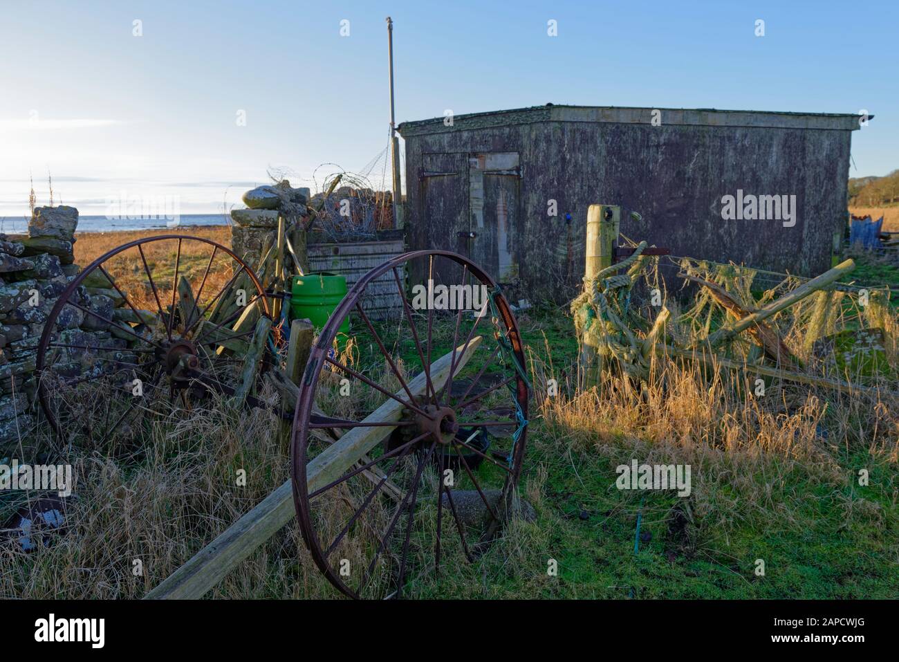 A pair of old metal rusting carriage wheels seen parked behind a stone wall next to a small Farm Hut in disrepair in a field off the Coastal path. Stock Photo