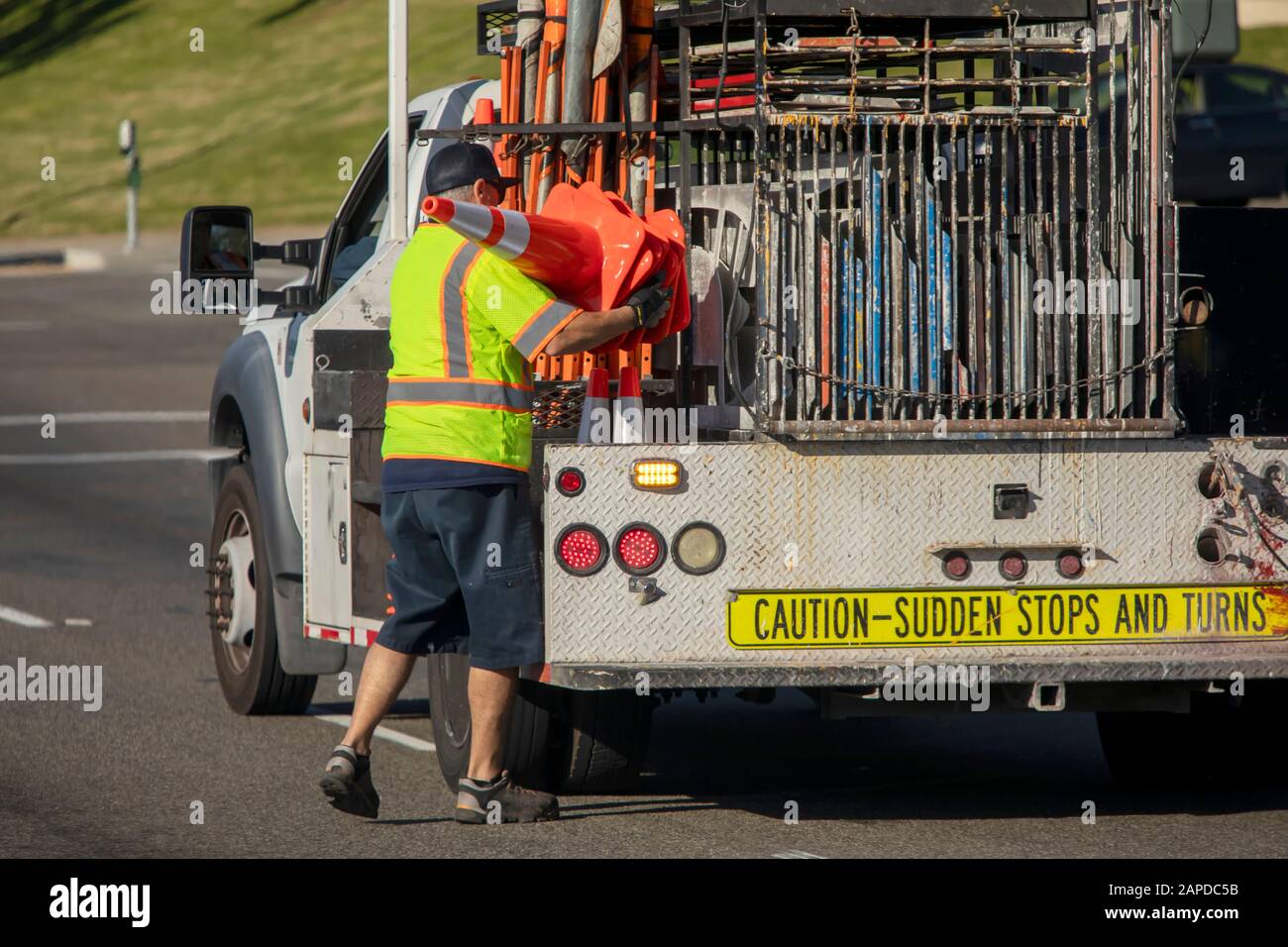 Worker behind utility truck placing bright orange traffic cones on roadway for traffic control Stock Photo
