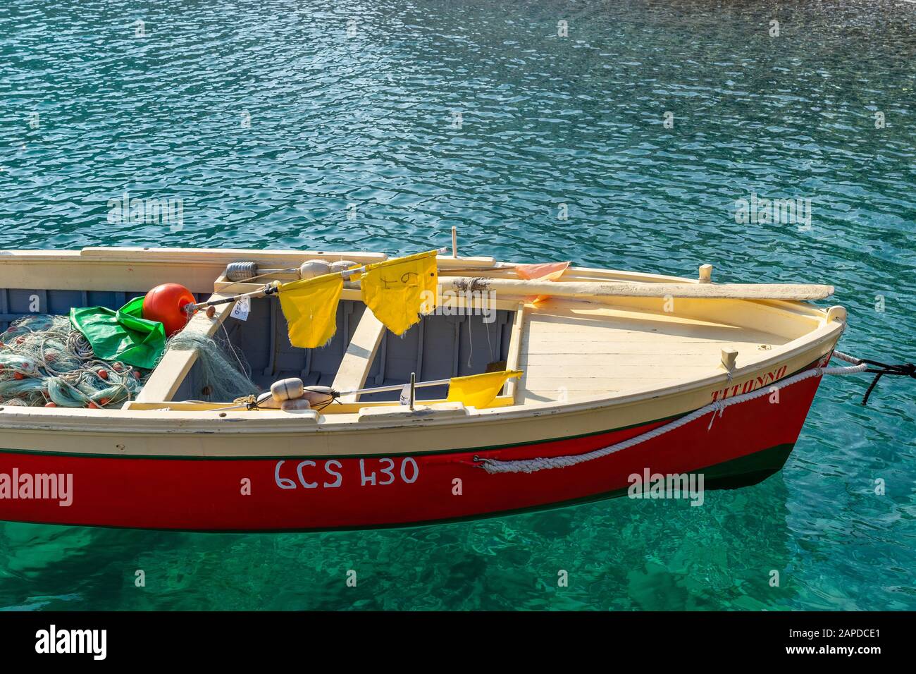 Part of a small fishing boat painted in bright red, beige and green colors in the blue water of the Mediterranean coast on a sunny day. There are padd Stock Photo