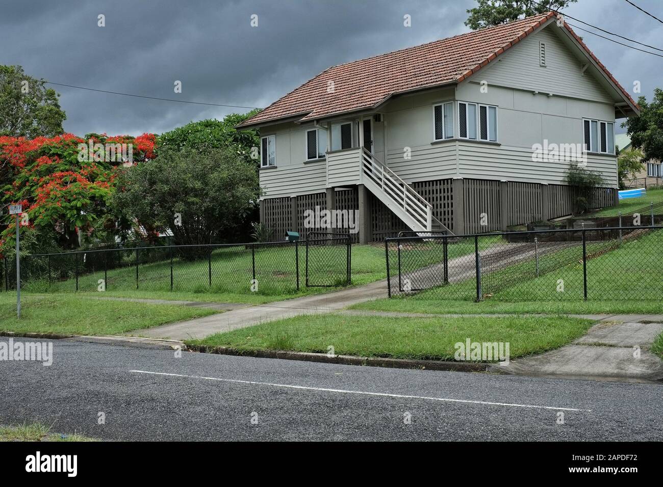 Lush green grassy front yard and a typical box shaped fibro and weatherboard post-war workers house with a poinsettia tree, Camp Hill, Brisbane Stock Photo