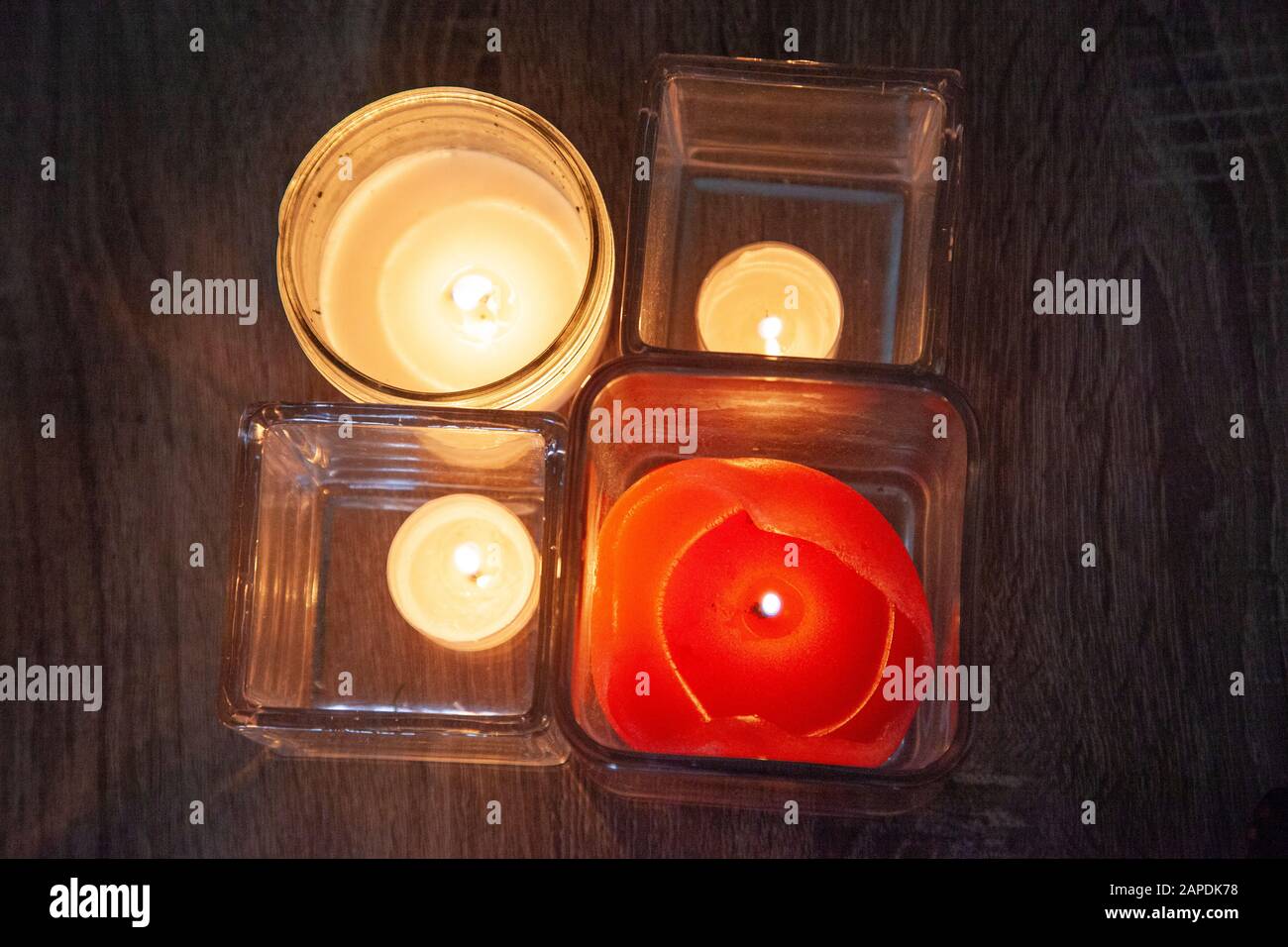 four candles lit and flicker inside glass holders in the darkness Stock Photo