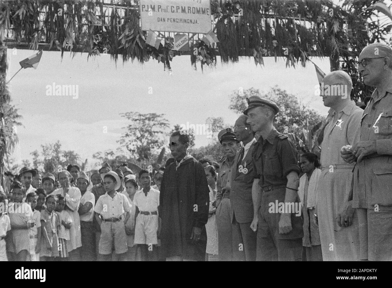 Visit Minister Romme to Great East [Makassar, Menado, Ambon, Flores, Surabaya] Description: Ambon. Reception Christian negory. Dr. C.P.M. Romom local female choir. Left next to him resident Fishermen, in addition an older man in costume with distinction (sengadji?) Annotation: At the welcome gate hangs a sign on which to read trap. P.J.M. Prof. C.P.M. Romme dan pengiringnja), Fully right Volkskrant journalist W. Snitke Date: 30 January 1947 Location: Indonesia, Dutch East Indies Personal name: Romme, C.P.M. Stock Photo