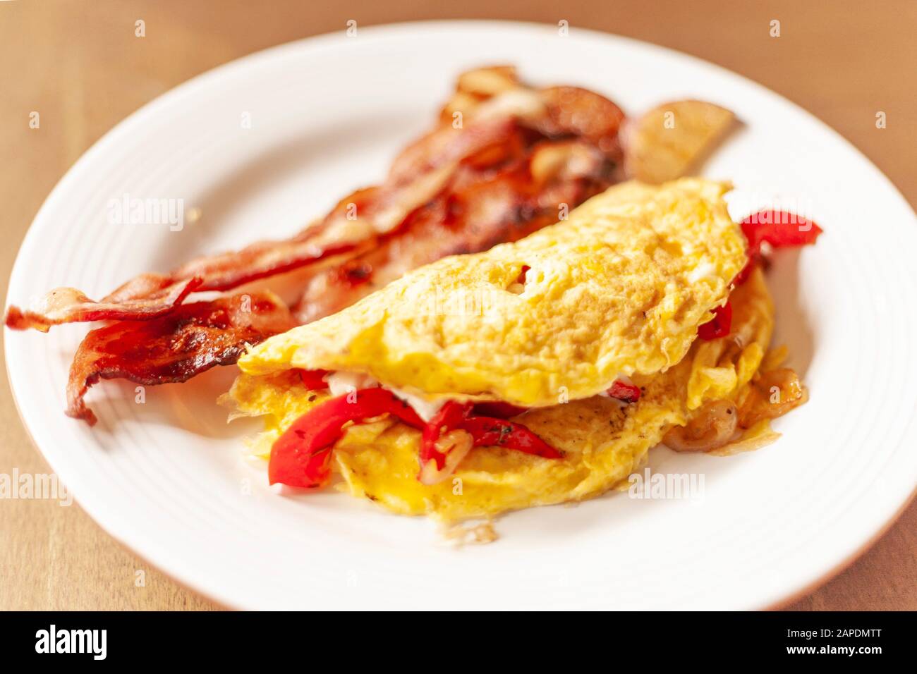An omelette with sauteed bell peppers, shallots, and sour cream is plated on a white dish with a wooden table as background. Stock Photo