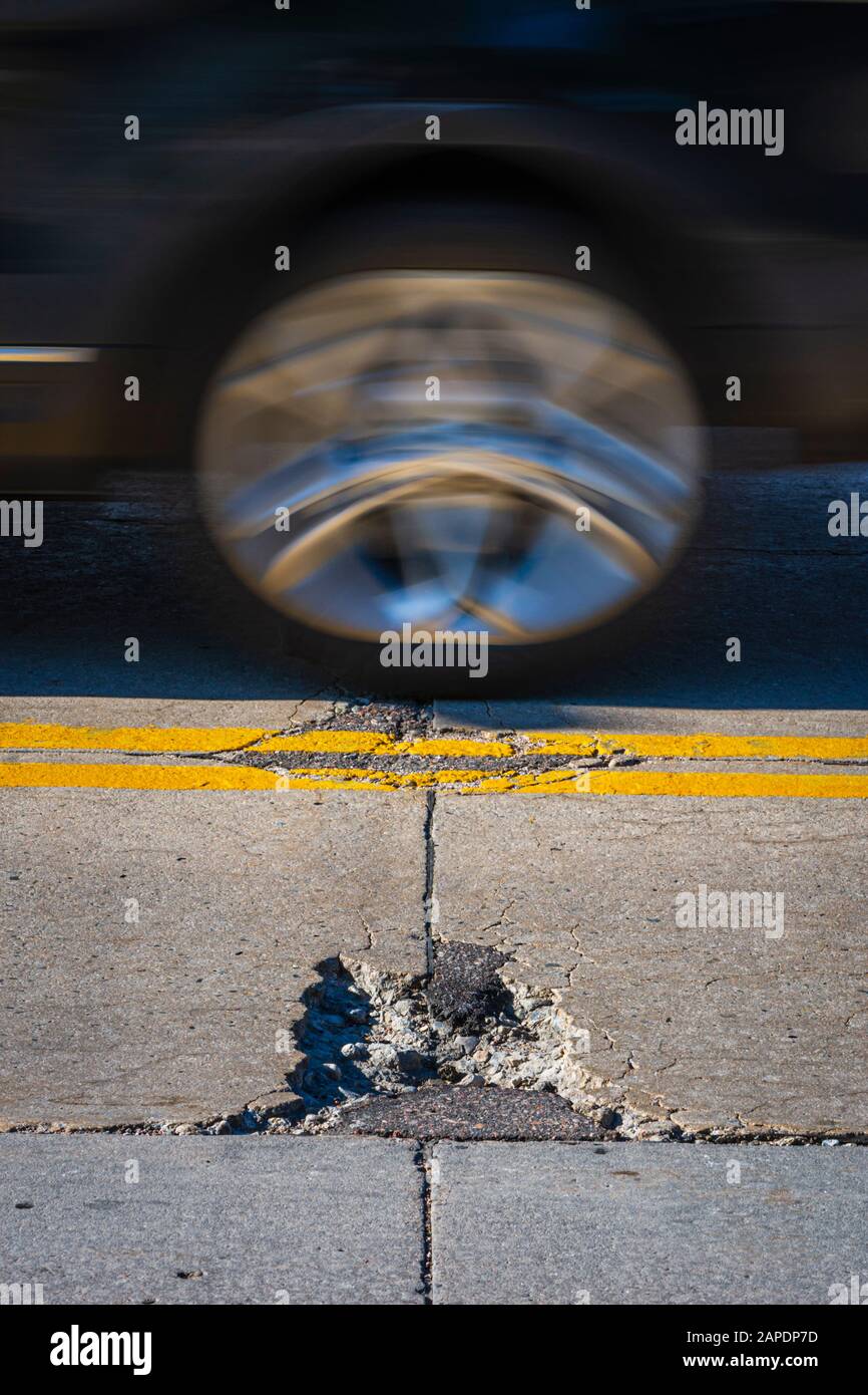 Old worn concrete road highway pavement in disrepair showing cracks,  repairs and chuck hole as auto passes by, Castle Rock Colorado USA. Stock Photo