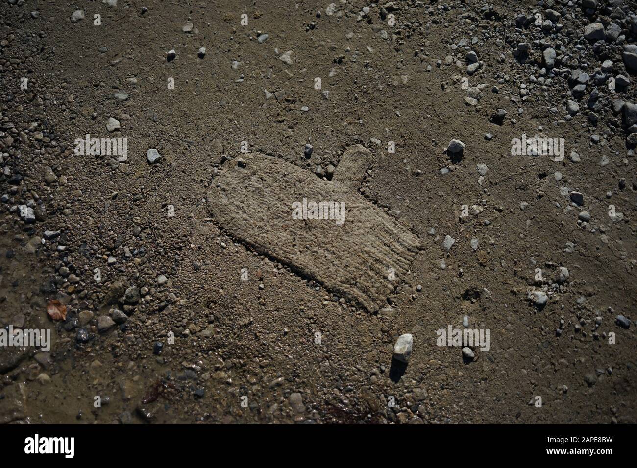 Mitten almost buried in soil surrounded by many rocks Stock Photo
