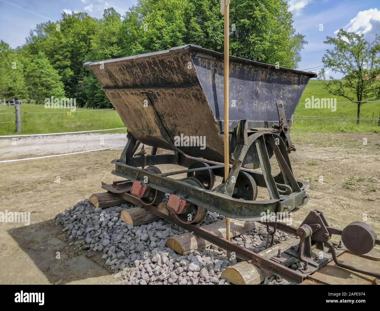 Old mine cart on tracks at daytime with a grassy field in the background Stock Photo