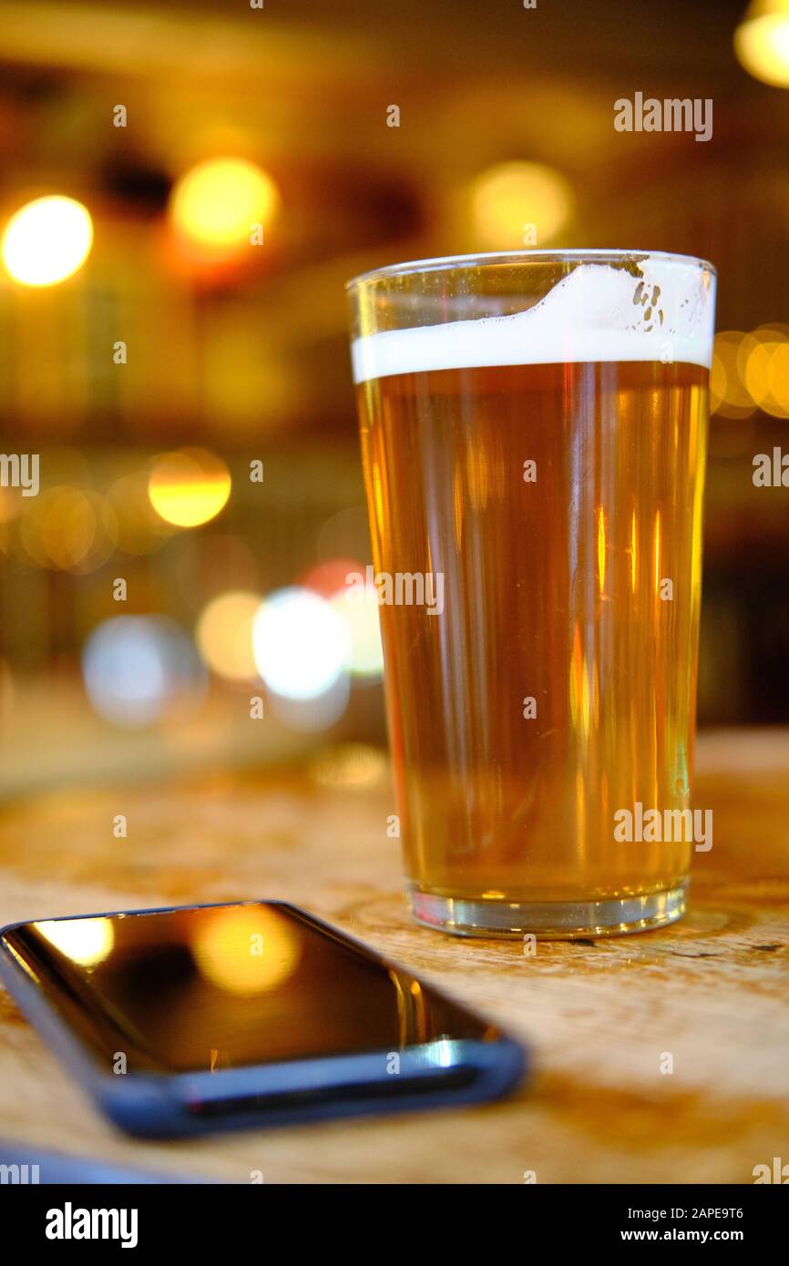 Closeup of a glass of beer on the table near a phone under the lights with a blurred background Stock Photo