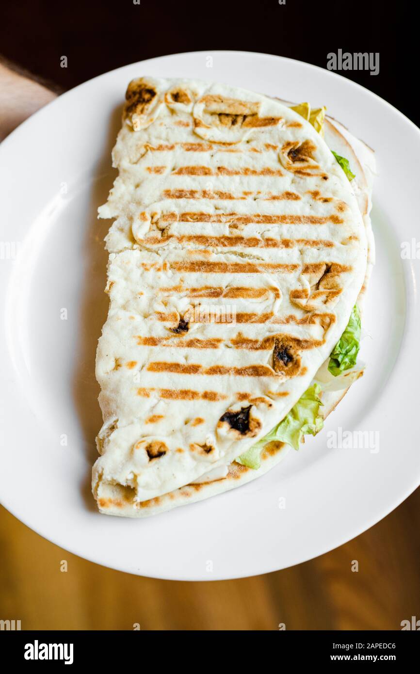 Panini Grilled Pita bread sandwich with turkey meat, Swiss cheese, lettuce on a white plate top down Stock Photo