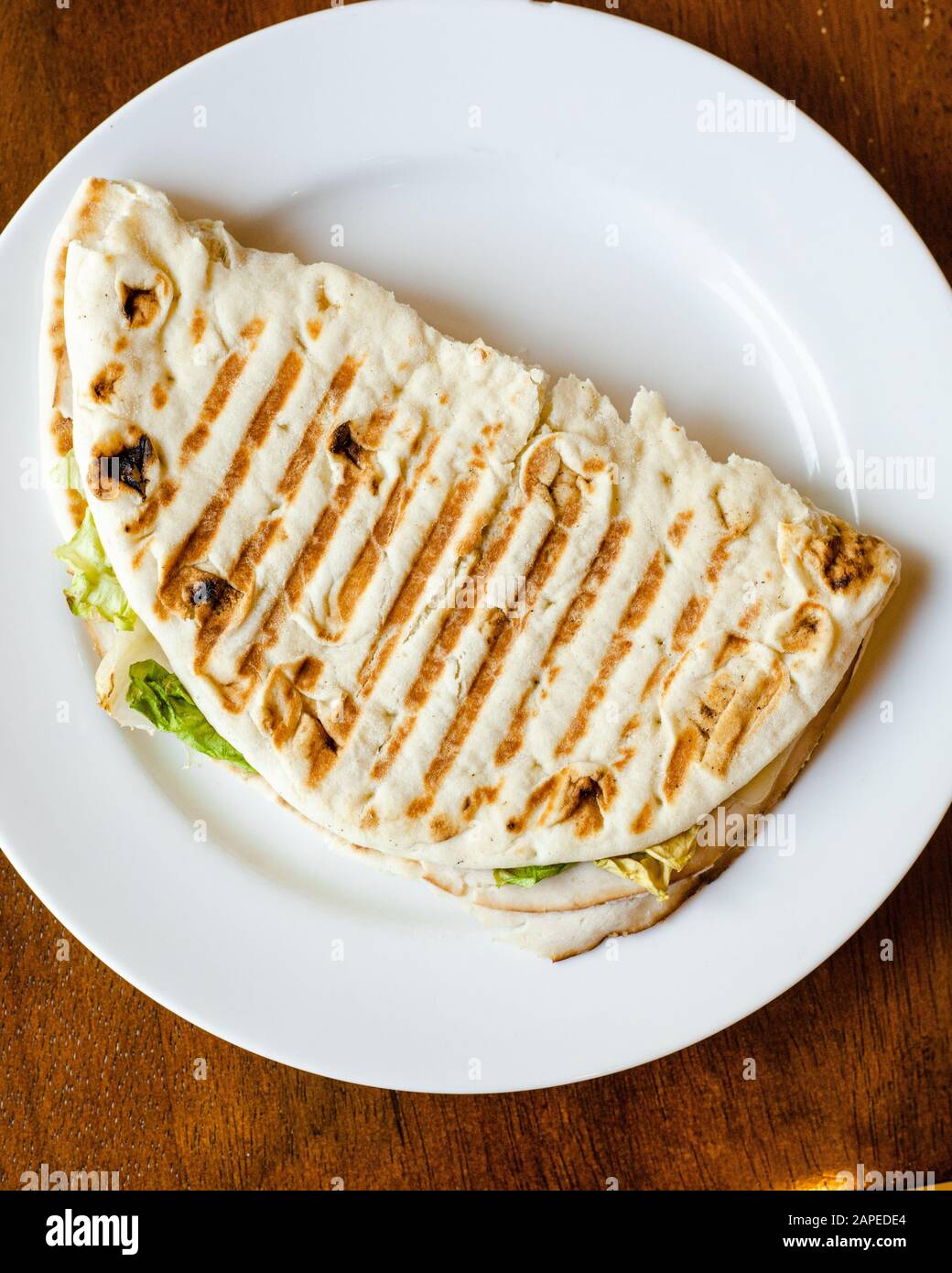 Flatbread Pita bread grilled panini sandwich folded in half with lettuce, turkey, melted cheese on a white plate top down Stock Photo