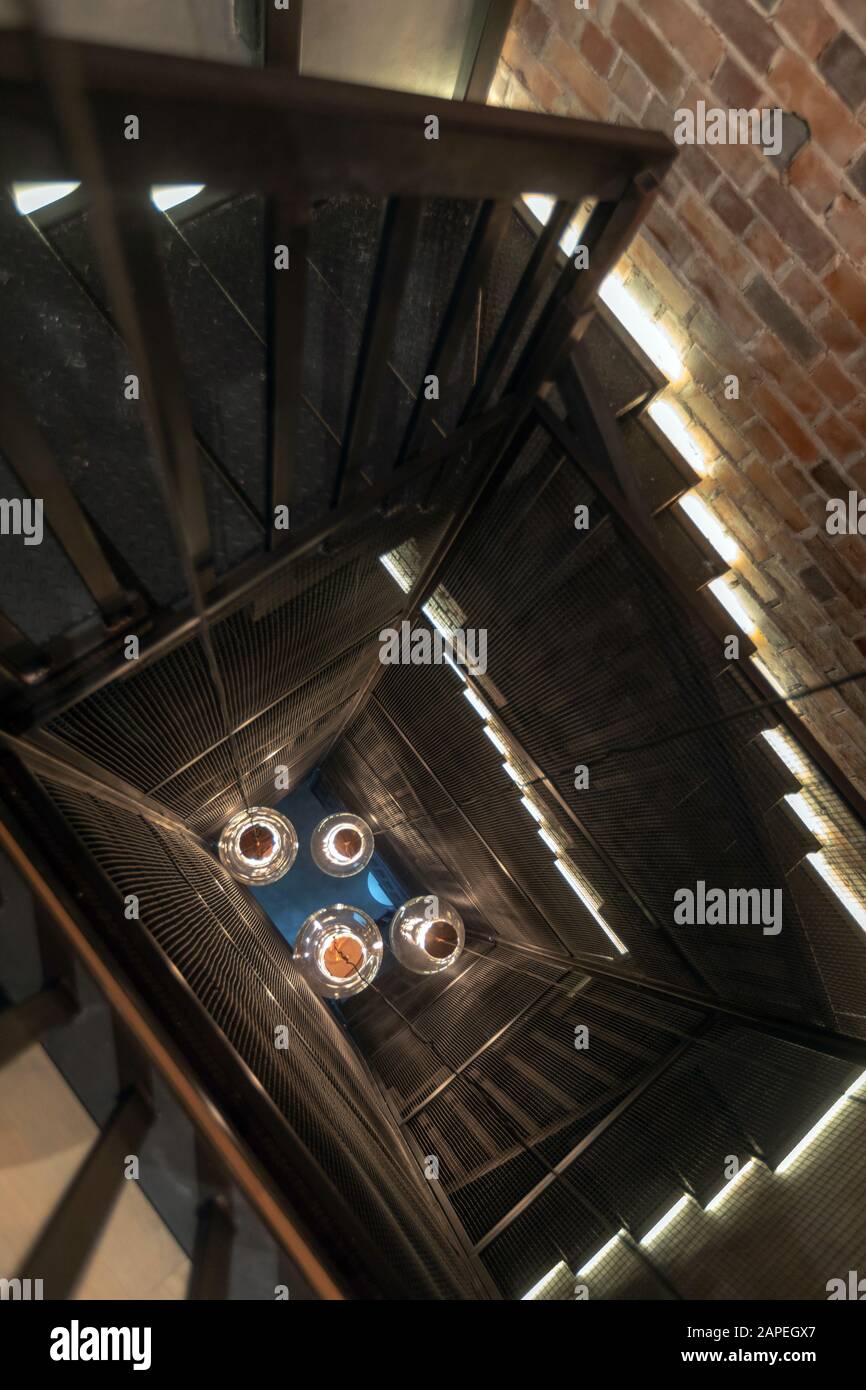 Giant pendant lamps in center of spiral staircase with red brick wall Stock Photo