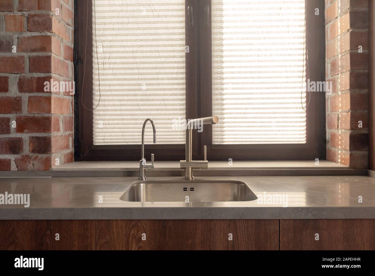 Kitchen sink with few faucets next to window and brick wall Stock Photo