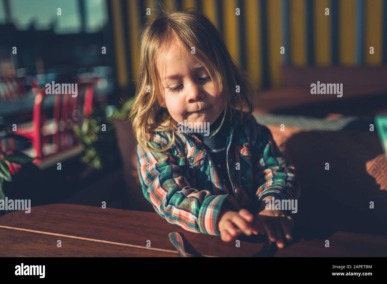 A little toddler is sitting at a cafe table with cutlery in front of him Stock Photo