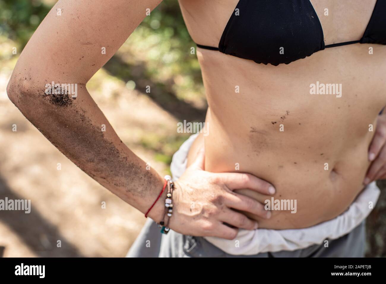 Female body, hand, stomach are dirty with earth and soot from a campfire, in a camp on a sunny summer day. Stock Photo