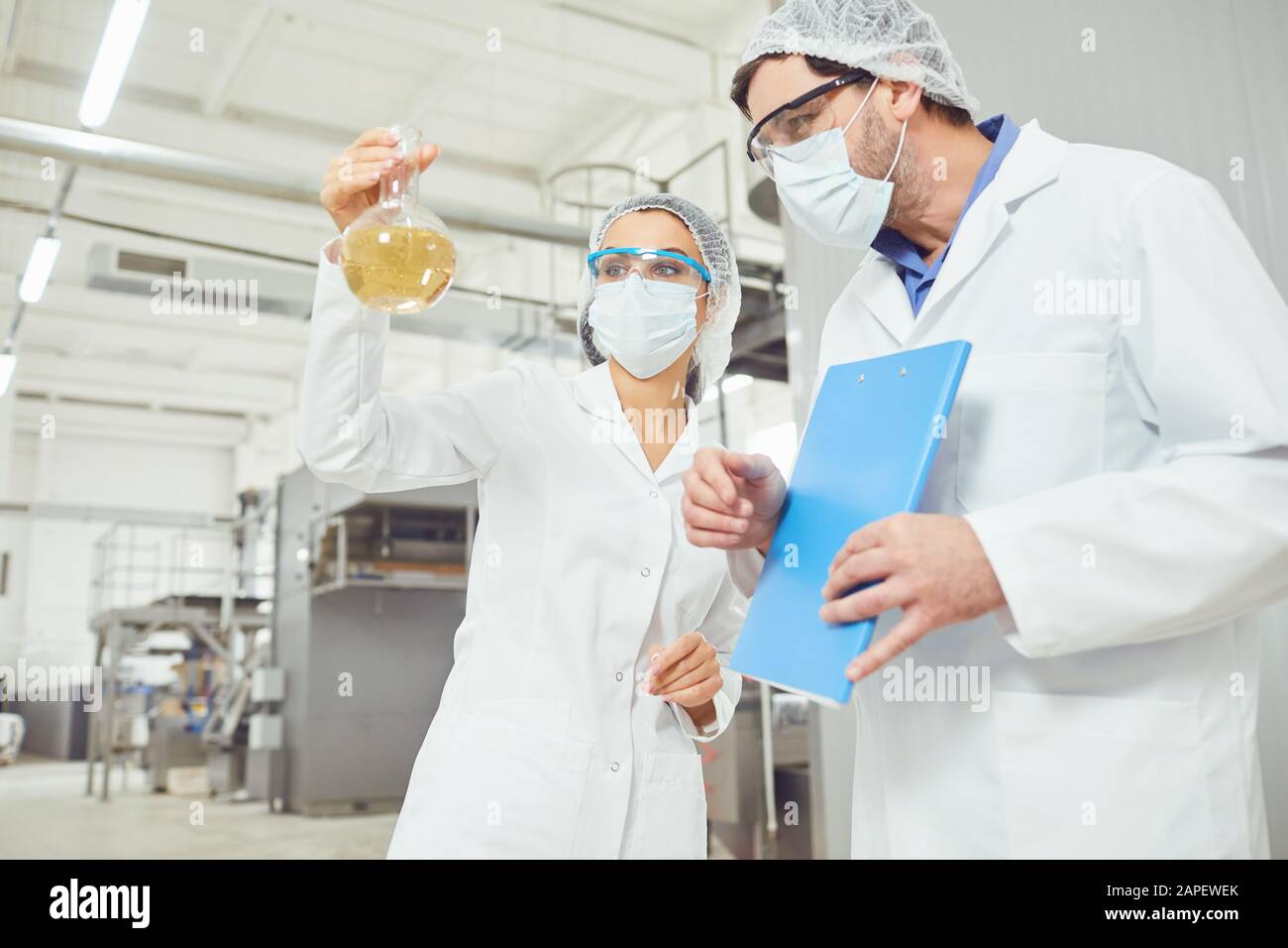 Workers in masks and coats look at the liquid in the flask at work Stock Photo