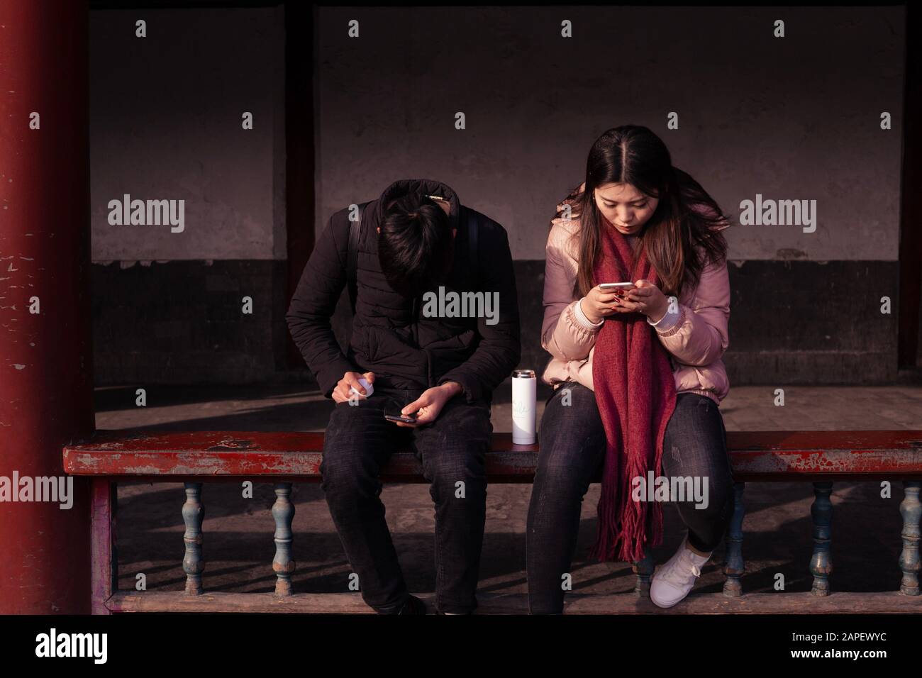 Millennials and technology / technology disrupting relationships. A young couple use phones to text, message and browse social media while seating Stock Photo