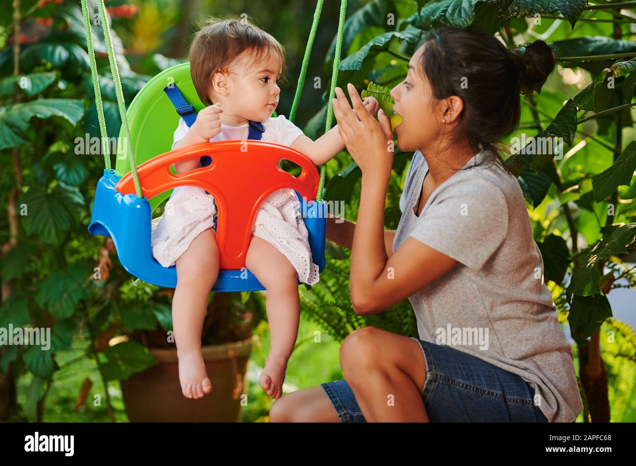 Young woman play with baby girl on swings Stock Photo