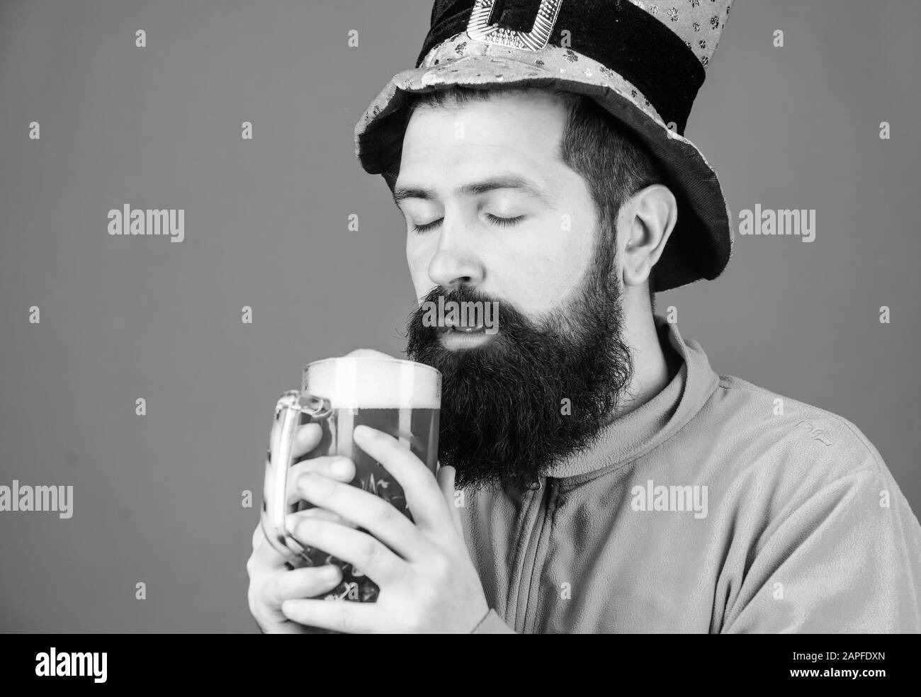 Quench his thirst with glass of cold beer. Irish man with beard drinking green beer. Hipster in leprechaun hat holding beer mug. Bearded man toasting to saint patrick. Celebrating saint patricks day. Stock Photo