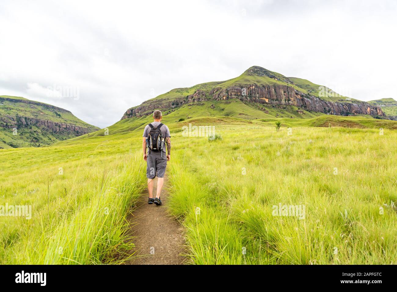 Man hiking on a small trail with a beautiful view to the green mountains of Maloti Drakensberg Park, Rainbow Gorge Trail, South Africa Stock Photo