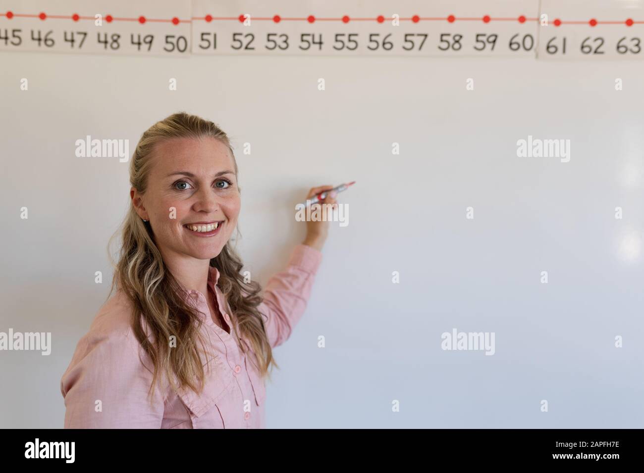 Female teacher with long blonde hair standing at a white board Stock Photo