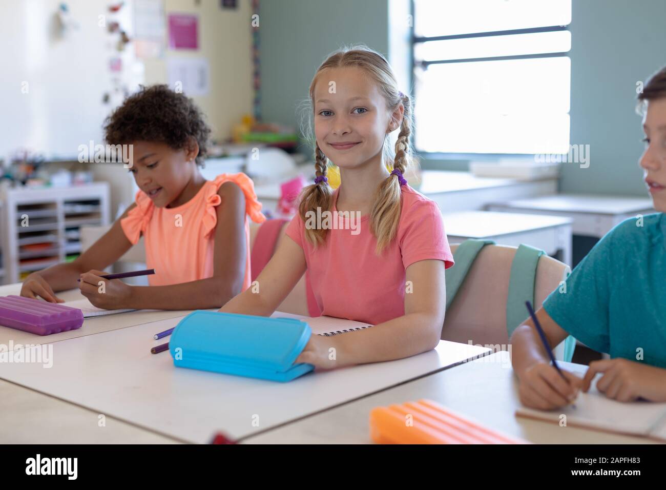Schoolgirl with blonde plaits sitting at a desk in an elementary school classroom Stock Photo