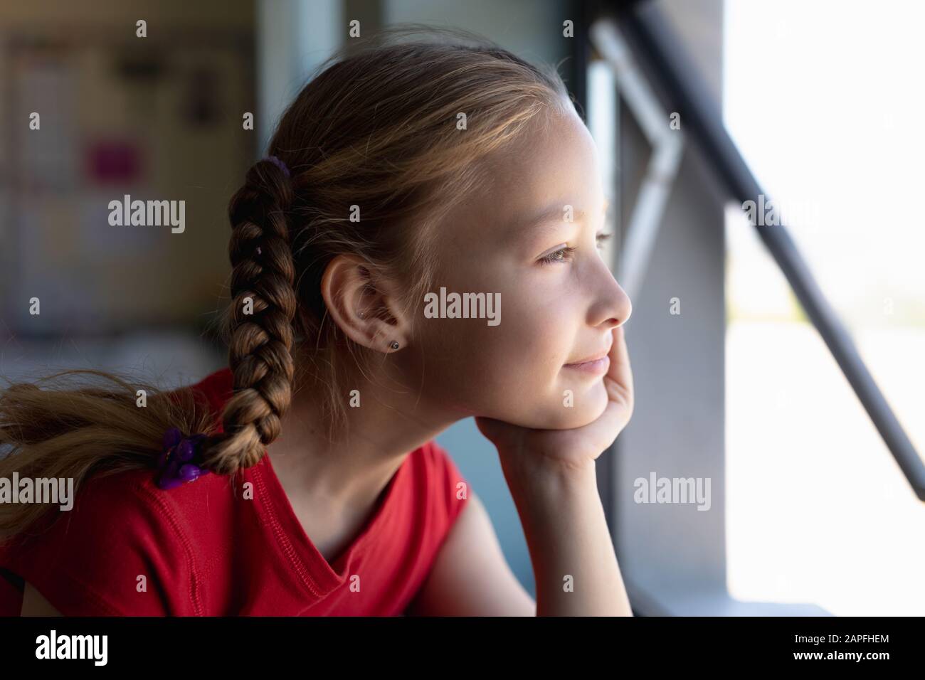 Schoolgirl looking out of an open window in an elementary school classroom Stock Photo