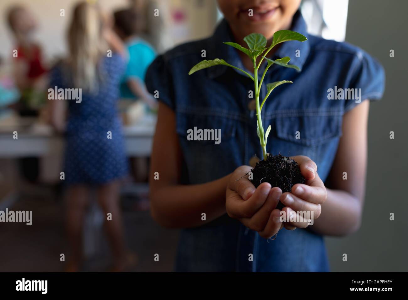 Schoolgirl standing holding a seedling plant in a jar of earth in an elementary school classroom Stock Photo