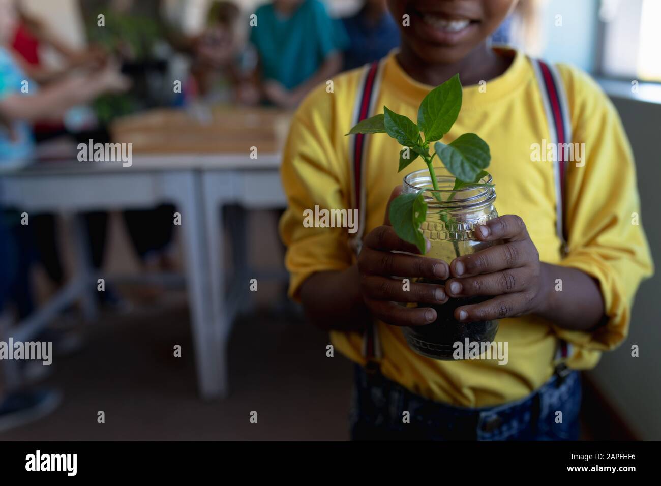 Schoolboy standing holding a seedling plant in a jar of earth in an elementary school classroom Stock Photo