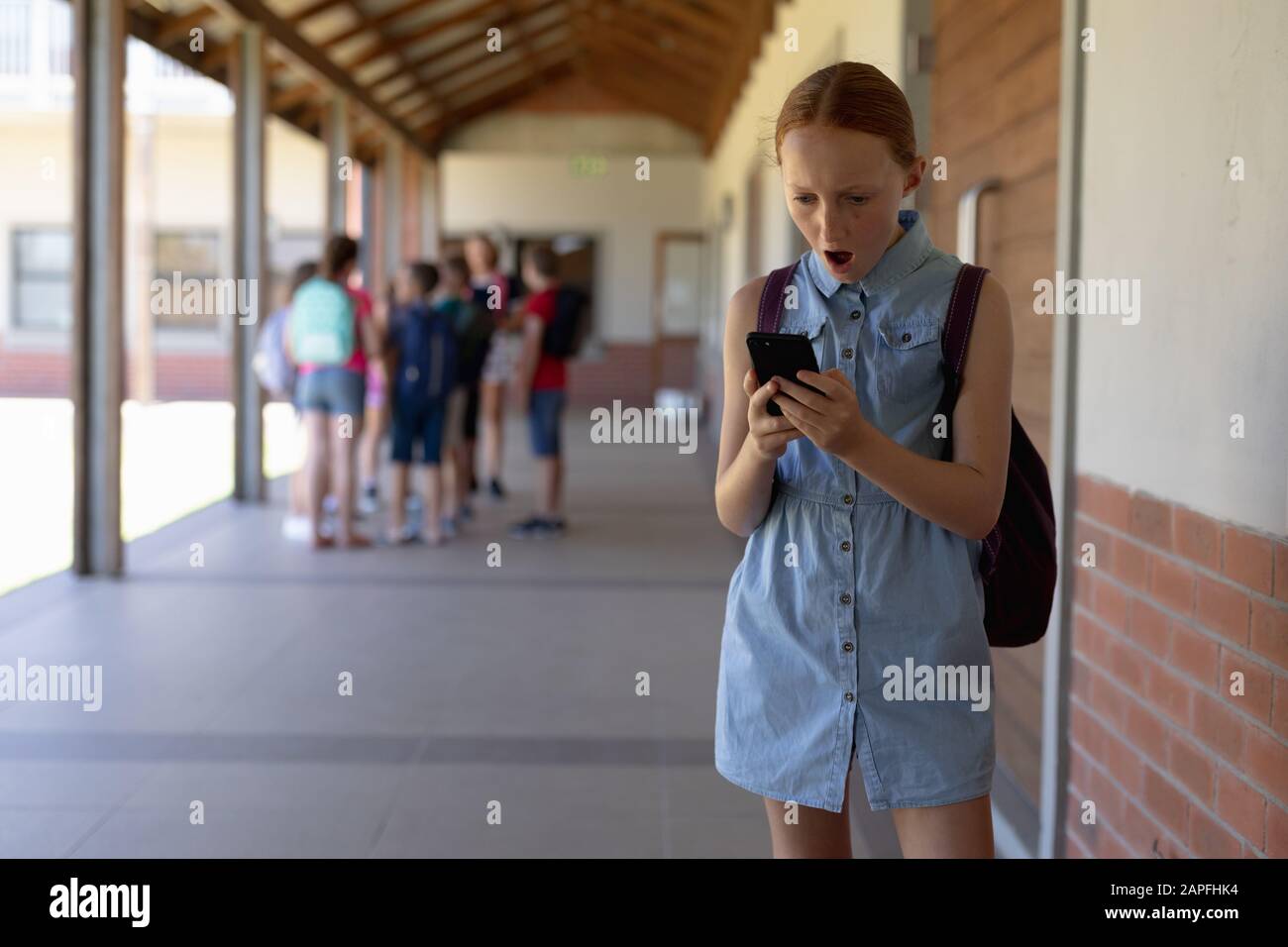 schoolgirl standing in the schoolyard at elementary school using a smartphone Stock Photo