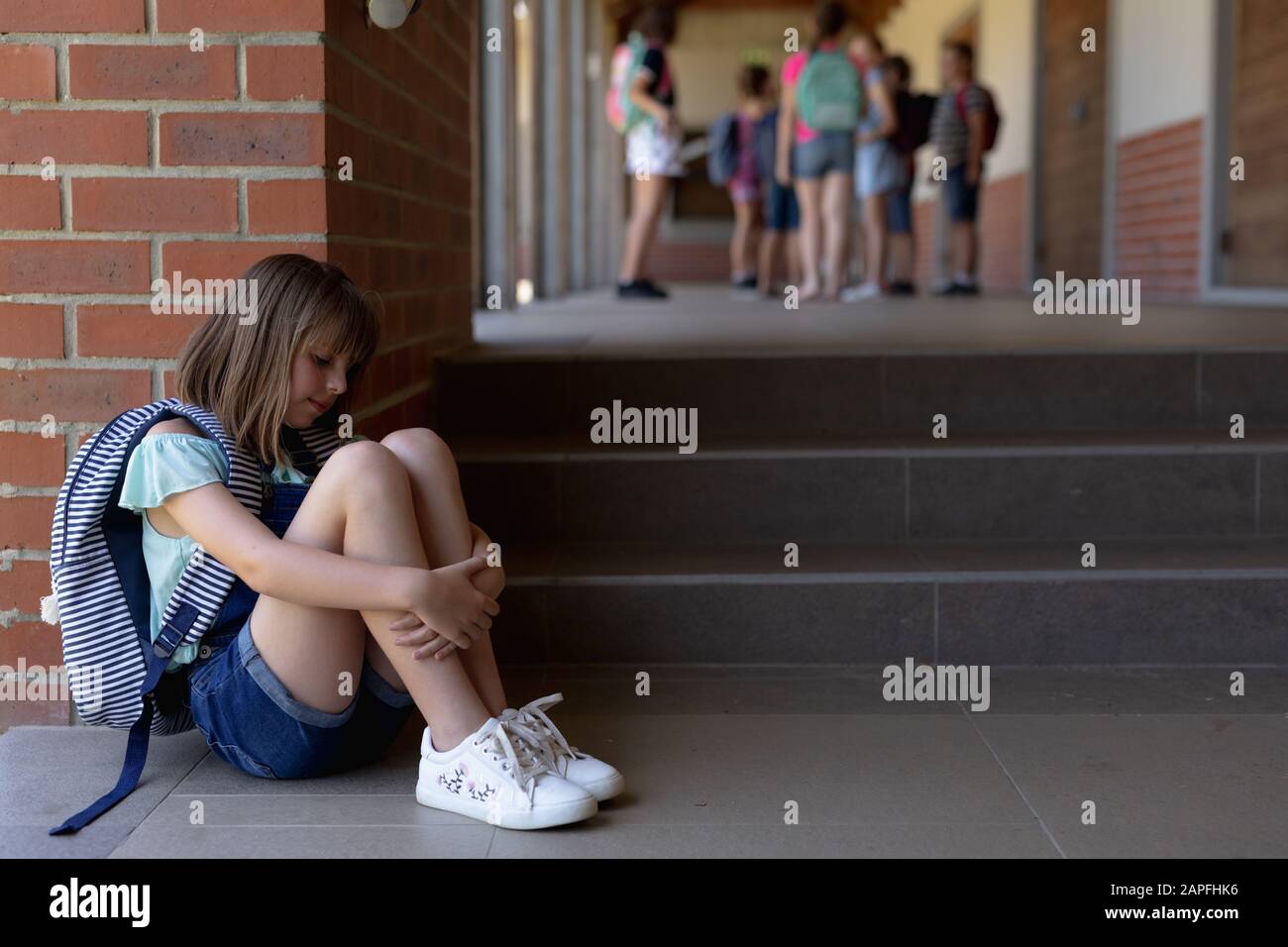 Schoolgirl  sitting on the ground alone in the schoolyard at elementary school Stock Photo