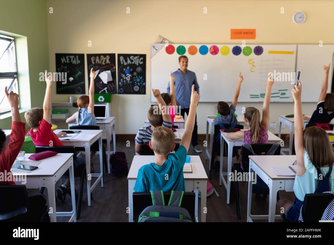 Male school teacher standing in an elementary school classroom with a group of school children Stock Photo